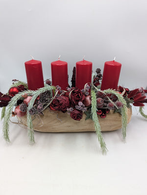 Längliches Adventsgesteck in Holzschale mit vier roten Stumpenkerzen, dunkelroten Rosen und Kiefernzweigen