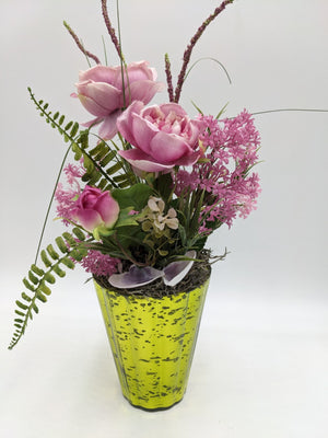 Sommergesteck mit rosa Rosen, Farnwedel, Gräsern und Muscheln in gelbgrünem Glastopf