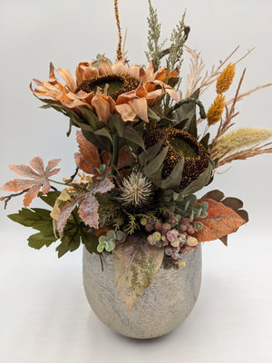 Gesteck mit zwei apricotfarbenen Sonnenblumen, Laub, Beeren und Gräsern in grauem Steintopf