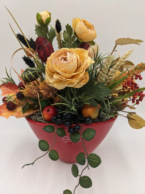 Herbstgesteck von vorn: gefüllte gelbe Rose, grüner Zierkürbis, Birnen, schwarze Beeren und Herbstlaub in roter Schale