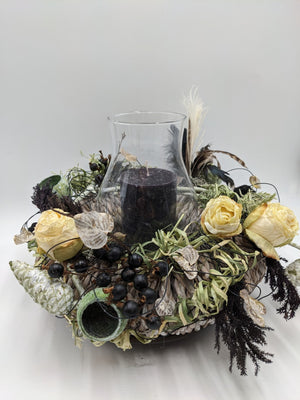 Herbstgesteck mit Glaswindlicht, schwarzer Kerze, cremefarbenen Rosen, schwarzen Beeren und Federn