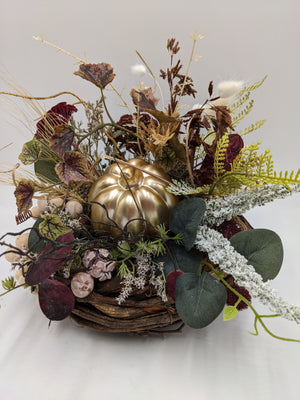 Herbstgesteck von oben: goldener Kürbis zwischen Eukalyptus, Farn, weiß bereiftem Zweig und beigen Kugeln