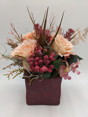 Herbstgesteck mit apricotfarbenen Rosen, roten Beeren und Gräsern in weinrotem quadratischem Topf