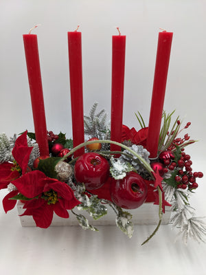 Nahaufnahme des Adventsgestecks mit glänzenden roten Äpfeln, silbernen Zapfen, Beerenzweigen und beschneiter Tanne