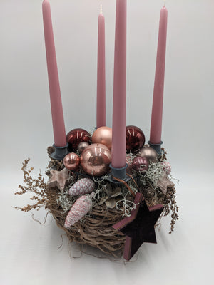 Adventsgesteck von der Seite: vier rosa Kerzen, Kugeln in Rosé und Altrosa, rosa Zapfen, Moos und Trockenzweige