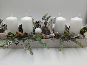Langes Adventsgesteck im weißen Holztablett mit vier weißen Kerzen, Schaukelpferd, grünen Kugeln und Zapfen