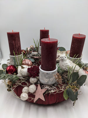 Adventsgesteck mit vier bordeauxroten Stumpenkerzen in grauen Haltern, rosé Kugeln, weißem Vogel und Eukalyptus