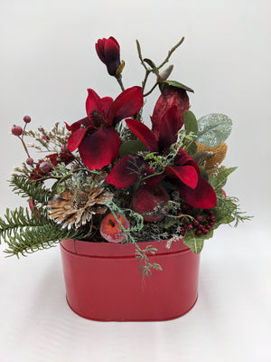 Wintergesteck mit dunkelroten Magnolien, gezuckerten Äpfeln, Banksia und Tannenzweigen in roter Metallschale
