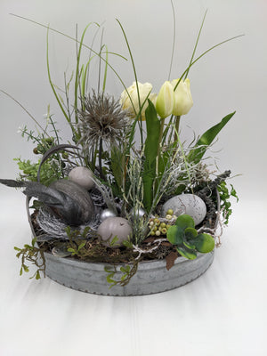 Ostergesteck in grauer Zinkschale mit cremeweißen Tulpen, Gräsern, Eiern in Grau und Silber sowie Moos