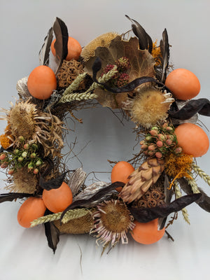 Türkranz in Orange und Natur mit Protea-Zapfen, Sonnenblumenboden, Beerenzweigen und Moos, schräg von vorn