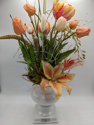 Hohes Frühlingsgesteck mit apricotfarbenen Tulpen, gelber Lilie, orangefarbenen Federn und Gräsern im weißen Pokal