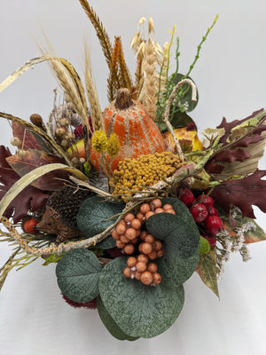Nahaufnahme des Herbstgestecks: Kürbis, senfgelbe Dolden, apricotfarbene Beerentraube und dunkelrote Eichenblätter