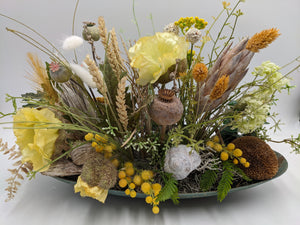 Flaches Sommergesteck in ovaler Schale mit gelben Mohnblüten, Ähren, Beerenkugeln und Schneckenhaus