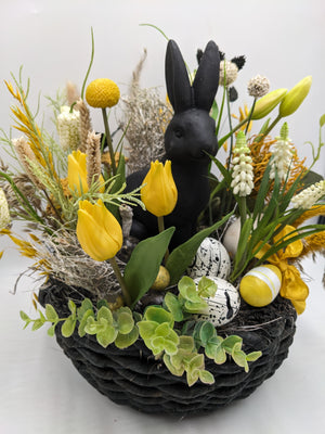 Ostergesteck von schräg oben: gelbe Tulpen, gesprenkelte Eier, gelbe Schleife und Eukalyptus am Korbrand