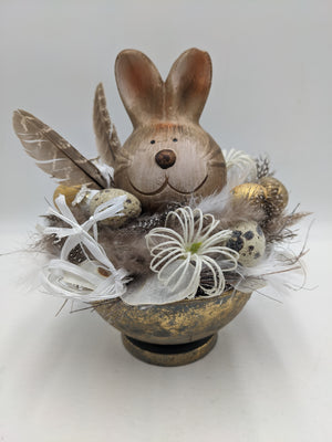 Ostergesteck in goldener Schale mit Keramikhase, Wachteleiern, weißen Spider-Blüten, Federn und Satinschleifen