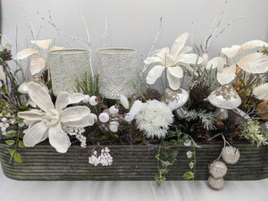 Langes Wintergesteck in Metallschale mit zwei silbernen Windlichtern, weißen Blüten, Pilzen und Zapfen