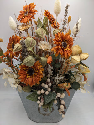 Gesteck von vorn: orange Gerbera, cremefarbene Blüte, Beerenzweige und Efeu über dem Rand des Zinktopfs