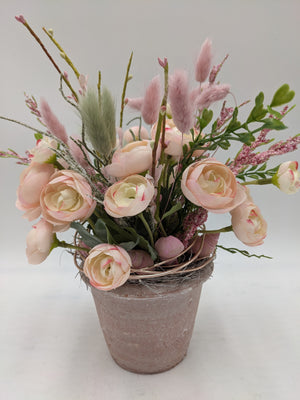 Sommergesteck mit rosa Ranunkeln, Hasenschwanzgras und Zweigen in grau-rosa Tontopf vor hellem Hintergrund
