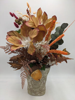 Herbstgesteck mit gelbbraunen Blüten, orangefarbenen Kolben, Farn und Zapfen in hellem Steintopf