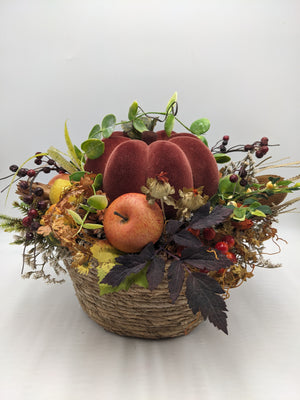Herbstgesteck im Naturkorb mit rotbraunem Samtkürbis, Apfel, Beeren und buntem Herbstlaub