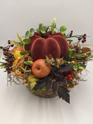 Herbstgesteck von vorn: Kürbis in Rotbraun, gelbe Birne, rote Beeren, Gräser und dunkles Laub im Korb