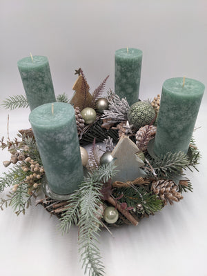 Adventskranz von oben mit vier grünen Kerzen, Silbersternen, Beeren, Zimtstangen und beschneiten Zweigen