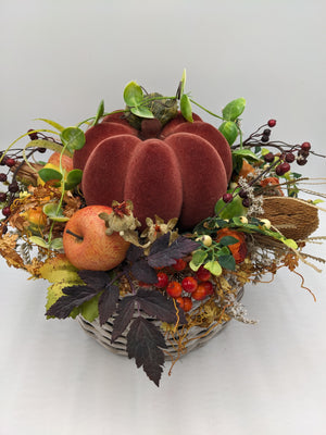 Herbstgesteck von schräg oben: Kürbis in der Mitte, ringsum Apfel, Beerenzweige, Gräser und Herbstlaub