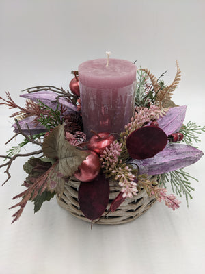 Tischgesteck in Rosa und Lila mit Stumpenkerze, Sedum, Heide, Zapfen und Beeren im grauen Korb von oben