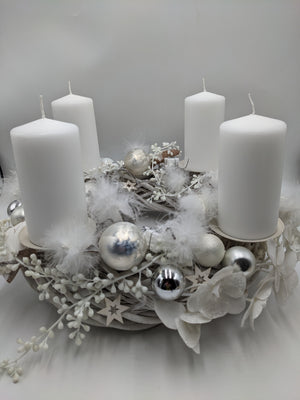Adventskranz in Weiß und Silber mit vier weißen Stumpenkerzen, Kugeln, Federn und Holzsternen, seitlich fotografiert