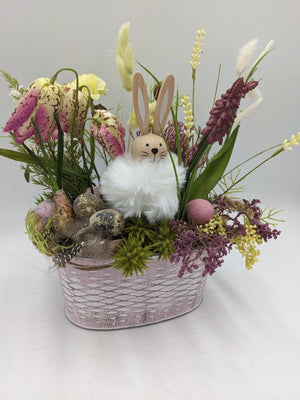 Frühlingsgesteck von der Seite: Hase mit Fellkörper, Moos, rosa Osterei und Trockenblumen in Rosa und Gelb