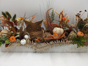 Langes Herbstgesteck im weißen Holzkasten mit Holzeule, weißen und orangen Kürbissen, Gräsern und Farnwedel