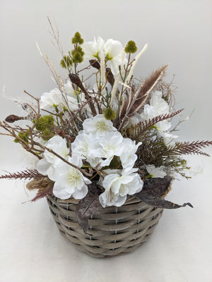 Frühlingsgesteck mit weißen Kirschblüten, Zweigen, Gräsern und grünen Kugelblüten im grauen Flechtkorb, von oben