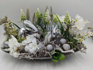 Ostergesteck in flacher Schale mit zwei silbernen Hasen, weißen Kirschblüten, Traubenhyazinthen und gesprenkelten Eiern