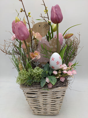 Ostergesteck im Weidekorb mit rosa Tulpen, Holzhase, weißem Osterei und feinen Zweigen