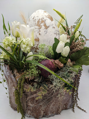 Frühlingsgesteck von vorn: weiße Tulpen, grüne Dolden, Farn und Eukalyptusranken um ein hohes Deko-Ei