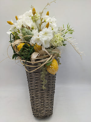 Wandgesteck im hohen grauen Korb mit weißen Kirschblüten, gelben Zitronen, Sukkulente und Gräsern