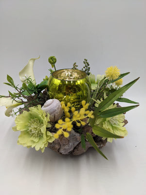 Sommergesteck mit gelbgrünem Windlichtglas, hellgrünen Blüten, weißer Calla und Schneckenhaus auf Rindentopf
