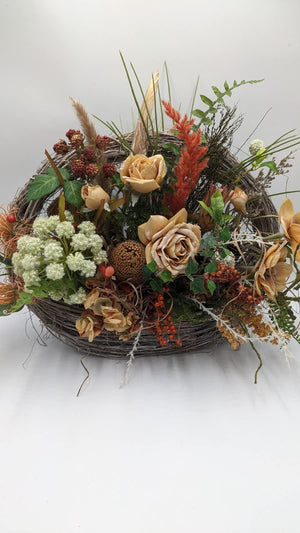 Herbstgesteck im Zweigkorb mit apricotfarbenen Rosen, Magnolie, Banksia, orangen Beeren und Gräsern