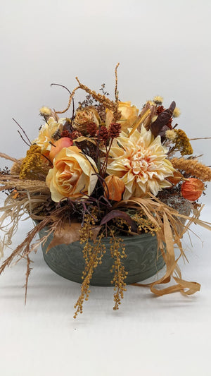 Herbstgesteck in graugrüner Schale mit gelben Rosen, cremefarbener Chrysantheme, Apfel, Zapfen und Gräsern