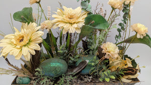 Nahaufnahme des Ostergestecks mit zwei grün glitzernden Eiern, Federn, Moos und cremefarbenen Blüten