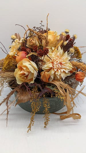 Herbstgesteck von vorn: Chrysantheme, Rose, orangefarbene Lampionblüten, gelbe Dolden und Bastbänder über dem Schalenrand