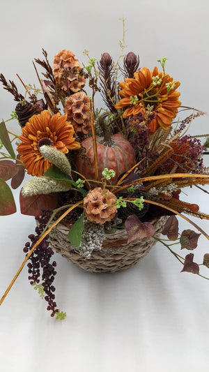 Herbstgesteck von vorn: Kürbis in Altrosa zwischen orangen Gerbera, Ähren, roten Blättern und hängenden Beeren