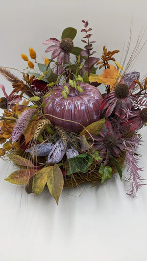 Herbstgesteck von vorn: glänzender Kürbis in Lila, umgeben von Ähren, Herbstblättern, Beeren und Efeu