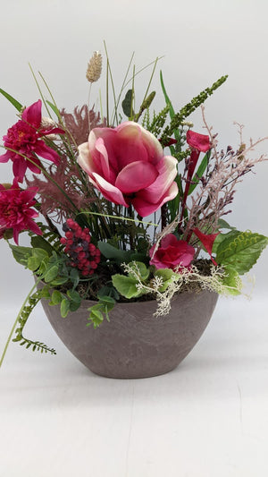 Tischgesteck in grauer Schale mit pinker Magnolie, Dahlien, roten Beeren und grünen Gräsern