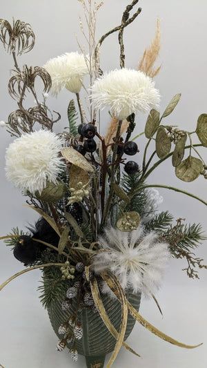 Nahaufnahme des Wintergestecks mit schwarzem Vogel, weißer Federblüte, goldgrünen Blättern und Gräsern