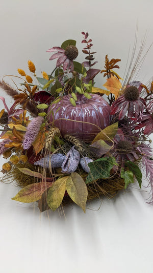 Herbstgesteck mit altrosa Kürbis, rosa Sonnenhut, Eukalyptus und Gräsern im Nest, seitlich fotografiert