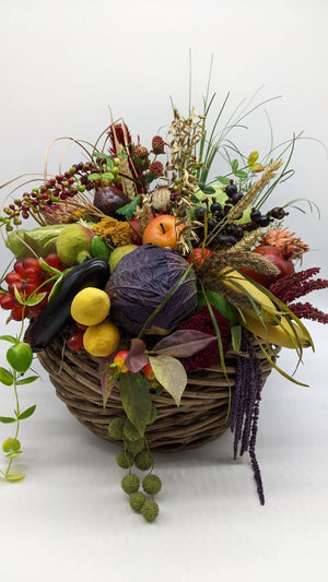 Herbstgesteck im Weidenkorb mit Rotkohl, Aubergine, Äpfeln, Zitronen, Beeren und Gräsern, seitlich fotografiert
