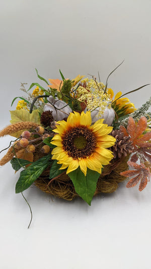 Herbstgesteck mit großer gelber Sonnenblume, zwei grauen Kürbissen, Hagebutten und Zapfen im Naturfasernest