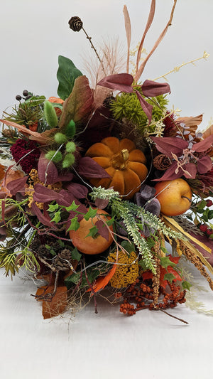 Nahaufnahme des Herbstgestecks mit orangefarbenem Samtkürbis, gelbem Apfel, weinrotem Laub und LED-Lichterkette