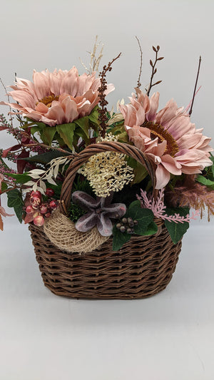 Korbgesteck von vorn: drei altrosa Sonnenblumen mit goldener Mitte, rote Blätter, rosa Beeren und Juteschlinge